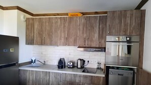 A modern kitchen with wooden cabinets, a stainless steel refrigerator, a built-in oven, and a coffee maker.