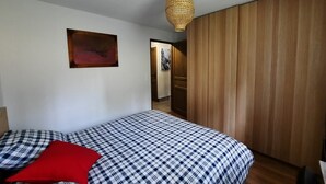 A bedroom with a bed, a red pillow, a wall-mounted picture, and a wooden wardrobe.