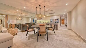 A spacious living area with a round dining table, modern pendant lights, and a kitchen in the background. - Beautiful New 3BR Condo at Indah (Puerto Vallarta)