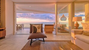 A modern living room with a view of the ocean, a sofa, a chair, and a dining area. - Beautiful New 3BR Condo at Indah (Puerto Vallarta)