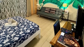 Ett hotellrum med en säng, en soffa, ett skrivbord och en vägg prydd med en stor väggmålning föreställande löv.
