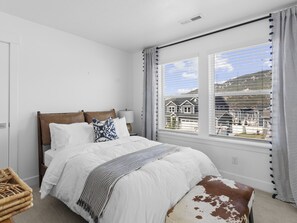 Enjoy a peaceful retreat with a view of the surrounding residential area from this cozy bedroom featuring a comfortable bed and stylish window treatments.