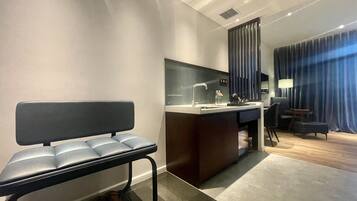 Une chambre d’hôtel moderne dotée d’un coin salon, d’un bureau avec un lavabo, d’un miroir et offrant une vue sur le paysage urbain.