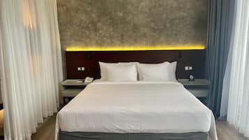 A modern hotel room with a large bed, a bedside table with a phone, and a nightstand with a clock.