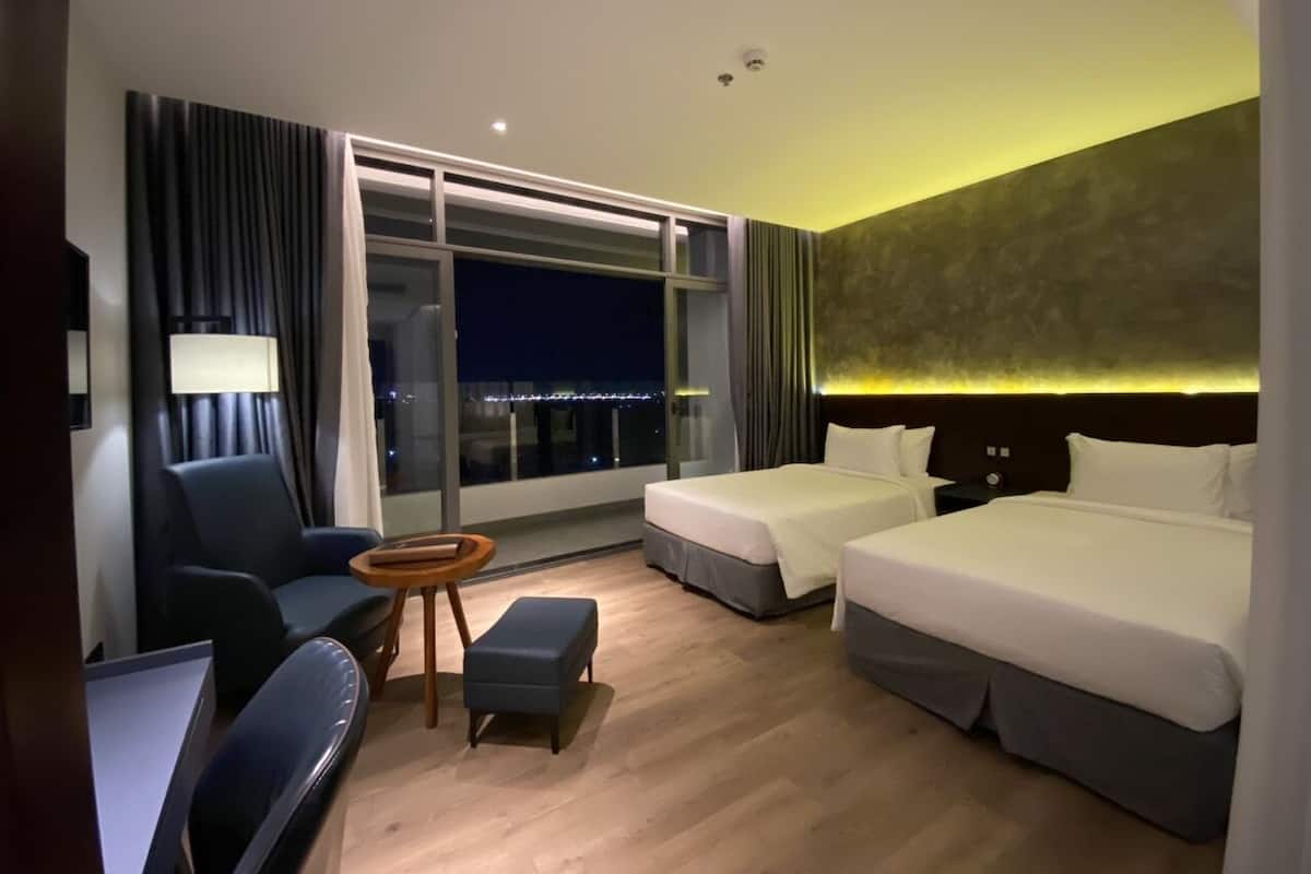 A hotel room with two beds, a desk, a chair, and a view of the city at night.