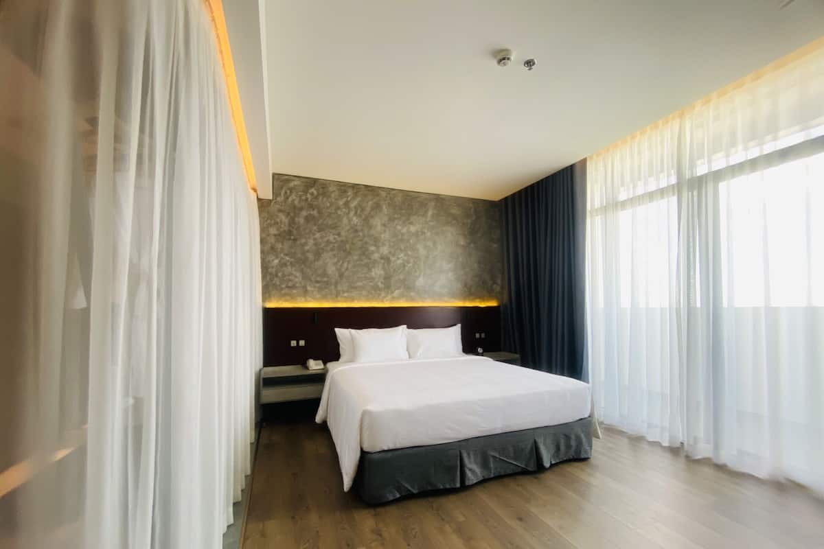 A modern hotel room with a large bed, a bedside table, and a headboard with a textured wall.