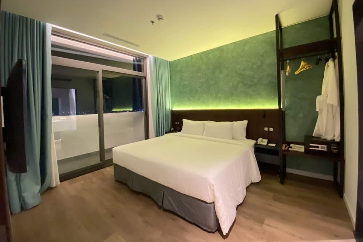 A hotel room with a large bed, a wardrobe, a mirror, and a view of the city at night.
