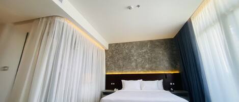 A modern hotel room with a large bed, a dark headboard, and a textured wall above the bed.