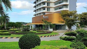 A modern hotel with multiple floors, a prominent 'NEWCC' sign, and a landscaped garden with neatly trimmed bushes and a roundabout. - NEWCC HOTEL & SERVICED APARTMENT (Truong Quang Trong)