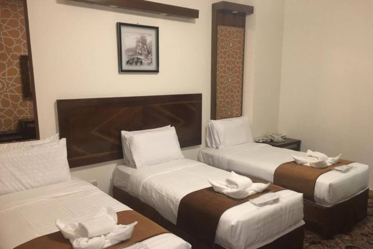 A hotel room with three single beds, each with white linens and brown headboards. There is a framed picture on the wall above the beds.