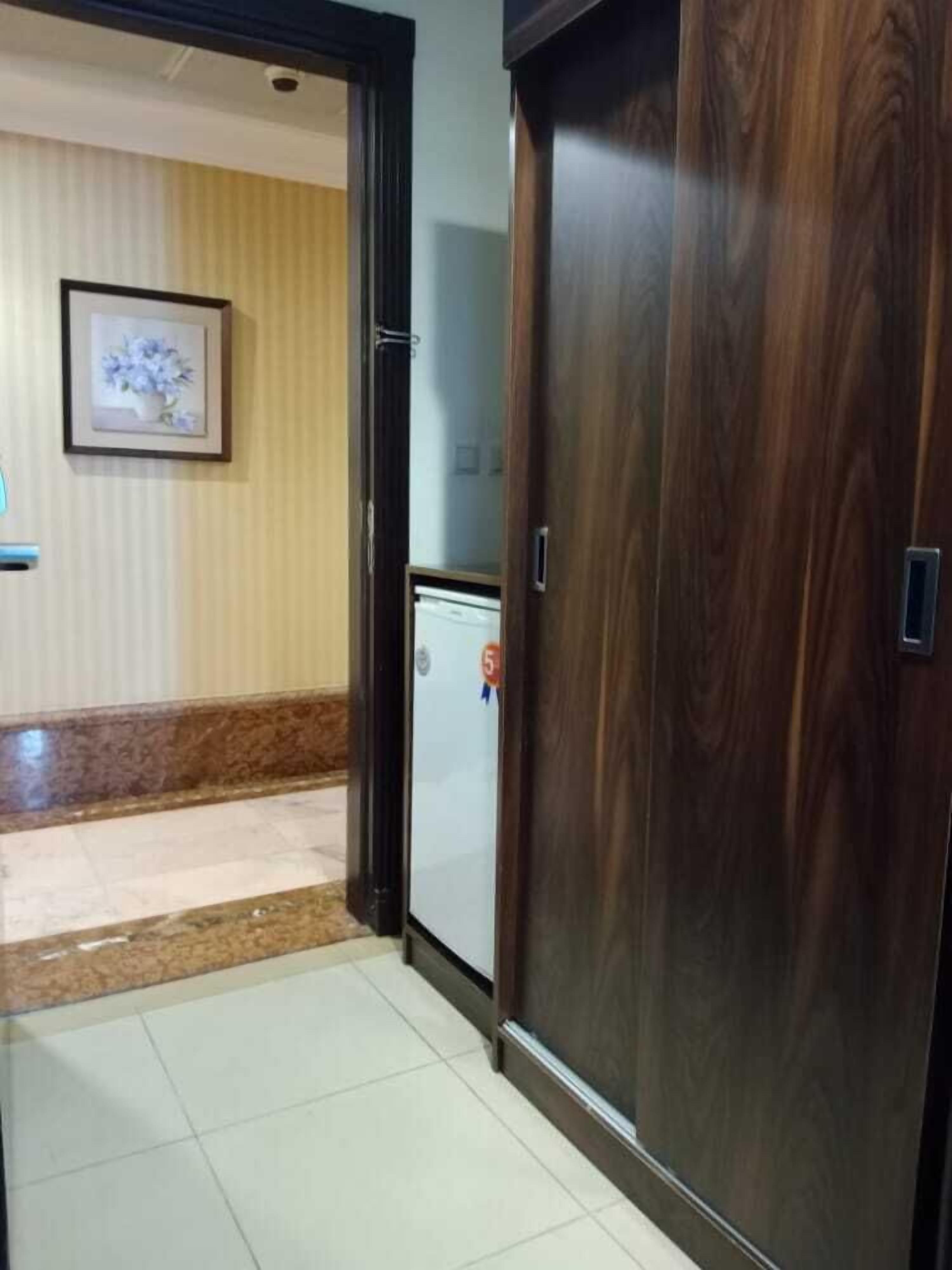 A hallway with a wooden door, a small refrigerator, and a framed picture on the wall.