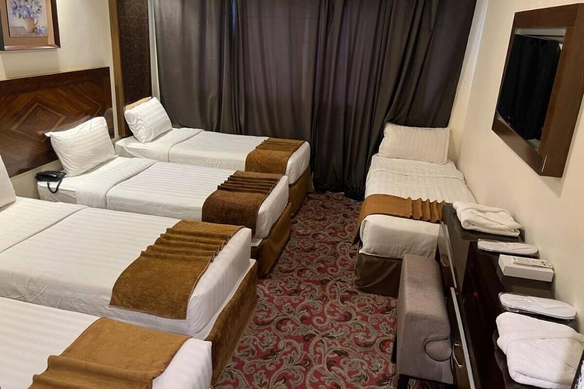 A hotel room with three beds, a desk with a chair, a small table with a mirror, and a red patterned carpet.