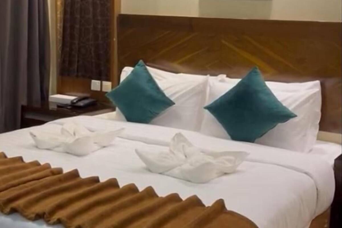 A neatly made bed with white linens, teal pillows, and a brown throw blanket.
