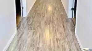 A hallway with wooden flooring and white walls, leading to a door with a small window.