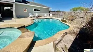 A swimming pool with a curved design, surrounded by a stone deck and a wooden fence.