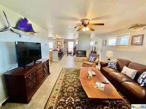 A spacious living room with a television, a ceiling fan, a coffee table, and a sofa. - 10th Street Lodge - Port O'Connor (Port O'Connor)