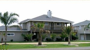 A two-story house with a balcony, surrounded by palm trees.