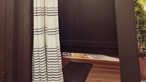 Un espace de douche extérieur en bois, agrémenté d’un rideau blanc à rayures noires.