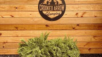 Eine Holzwand mit einem Logo, das "Crooked Arrow Glamping" zeigt.