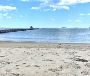 Una spiaggia sabbiosa con impronte che conducono a un molo roccioso.