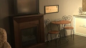 Una sala de estar con chimenea, dos sillas de metal, una mesita y un sillón estampado.