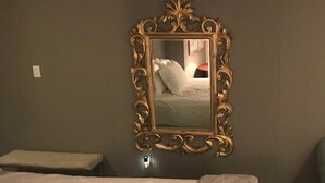 Habitación de hotel con una cama grande, una mesita de noche y un espejo adosado a la pared con un marco decorado.