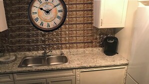Una cocina con un lavamanos doble, un reloj y una cafetera.