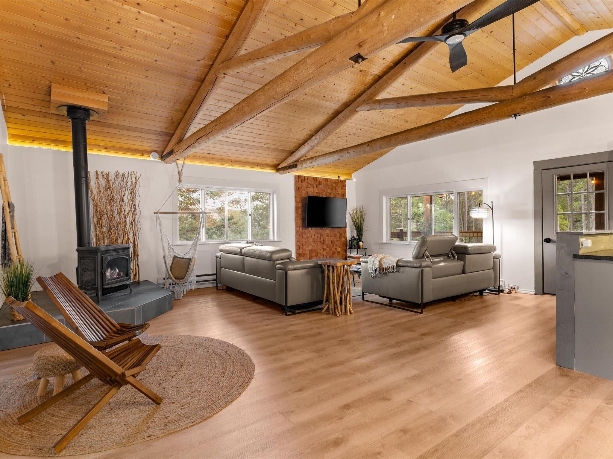 A spacious living room with a fireplace, two sofas, a wooden ceiling, and large windows.
