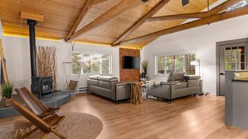 A spacious living room with a fireplace, two sofas, a wooden ceiling, and large windows.