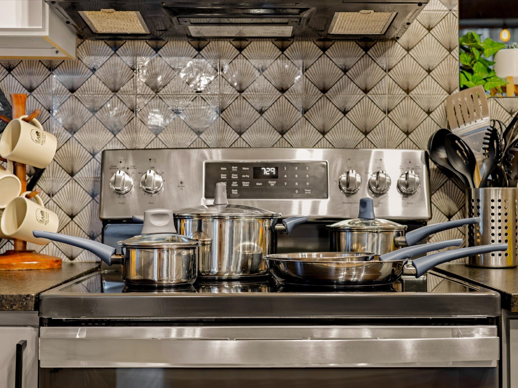 A kitchen with a stainless steel stove, pots, and a tiled backsplash.