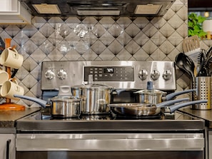A kitchen with a stainless steel stove, pots, and a tiled backsplash. - Open Air Cinema & Hot Tub | Restored Log Cabin (Conifer)