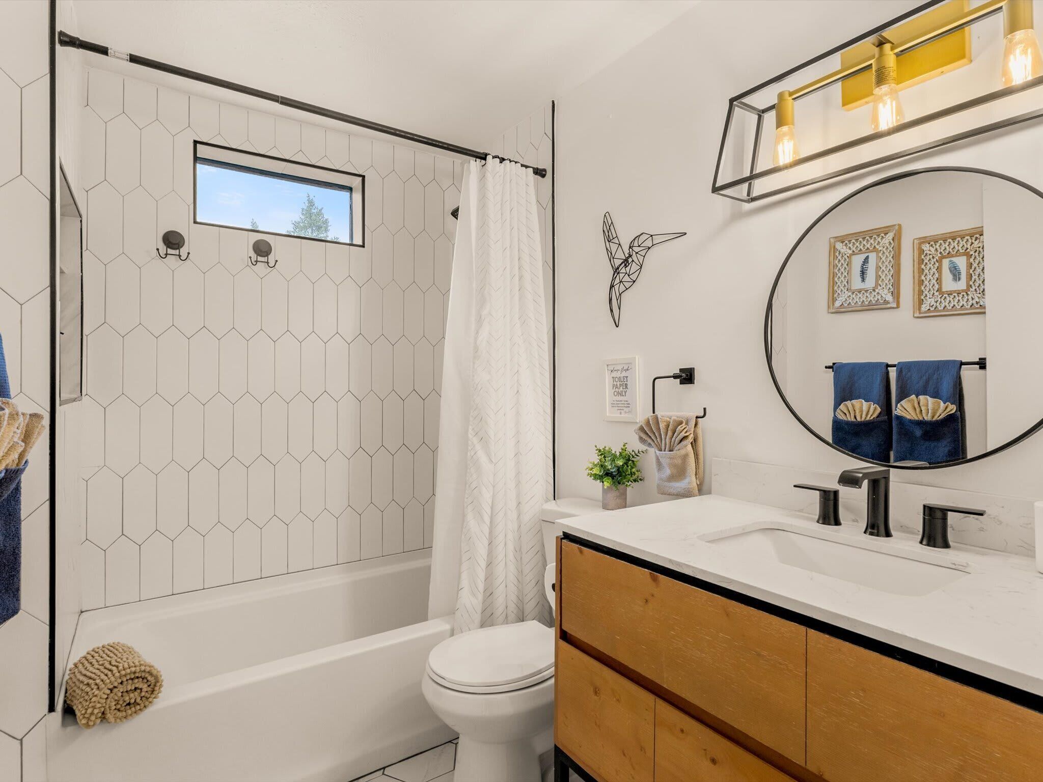 Een moderne badkamer met een wand betegeld met witte zeshoekige tegels, een bad, een toilet, een wastafel met spiegel en een handdoekhouder.
