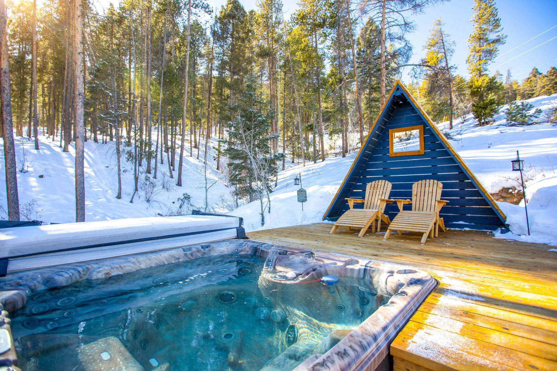 A wooden cabin with a hot tub and two Adirondack chairs on a deck.