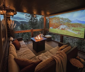 A cozy lounge area with a fire feature, comfortable seating, and a large screen displaying a nature scene.