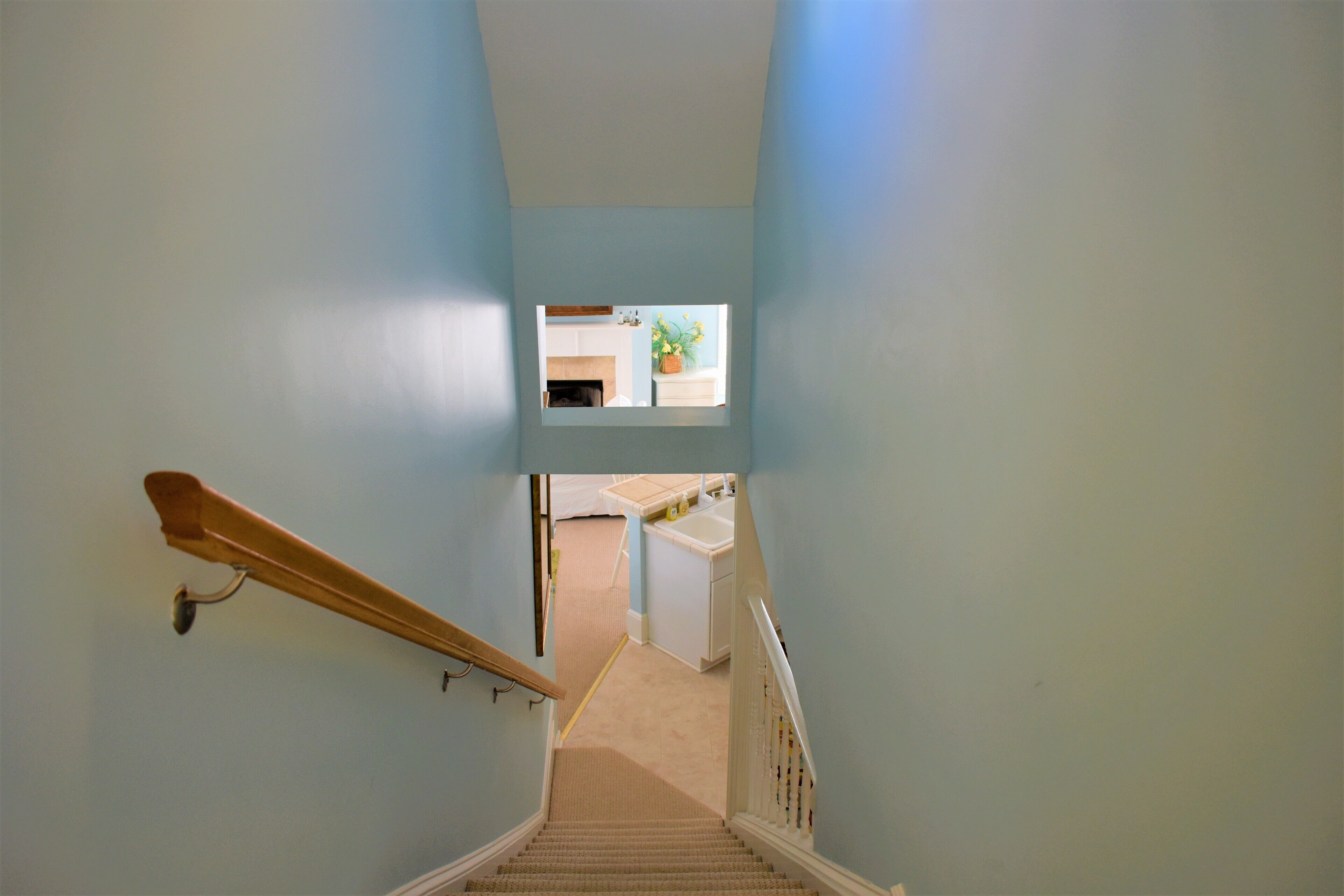 A narrow staircase with a wooden handrail and beige carpet.