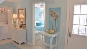 A room with a white dresser, a small table with a bowl, a door, and a window.