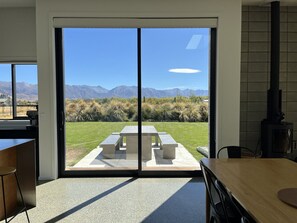 A modern kitchen with a large sliding glass door leading to an outdoor patio with a concrete table and benches, overlooking a mountainous landscape.