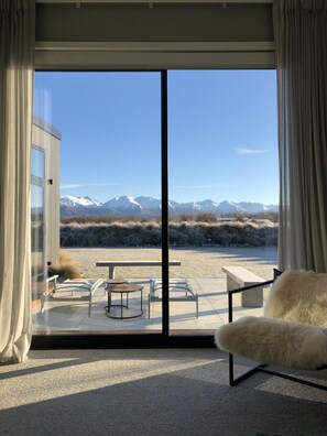 Une chambre moderne dotée d’une grande porte-fenêtre coulissante qui donne sur un patio extérieur. Le patio comprend une table et des chaises, et offre une vue sur des montagnes enneigées.