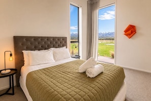 A bedroom with a large bed, a nightstand with a lamp, and a view of mountains through a window.
