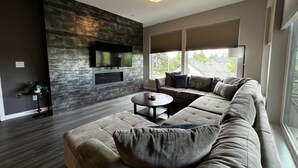 Ein modernes Wohnzimmer mit einem Ecksofa, einem Flachbildfernseher und einem Kamin.