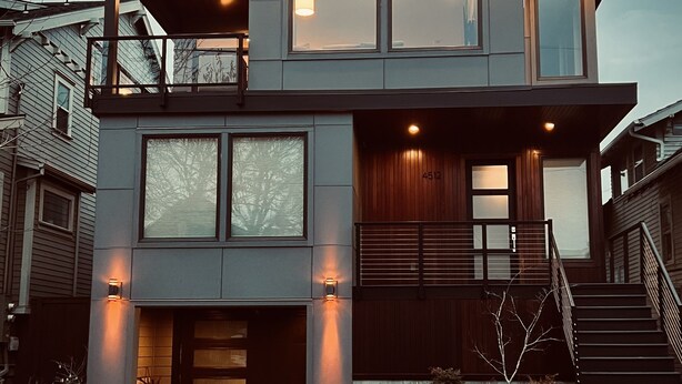 Ein modernes, zweistöckiges Haus mit Balkon, großen Fenstern und Hauseingang.