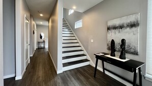 Ein moderner Flur mit Holzboden, einer Treppe und einer an der Wand befestigten Skulptur.