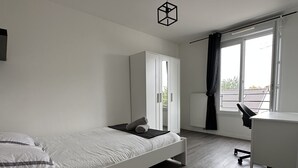 Un dormitori minimalista amb un llit individual, un armari blanc, una taula d'estudi i una finestra amb cortines.