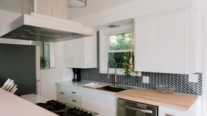 A modern kitchen with white cabinets, a black and white backsplash, a wooden countertop, and a stainless steel dishwasher. - Beautiful cottage w/pool in bamboo forest! (Central Point)
