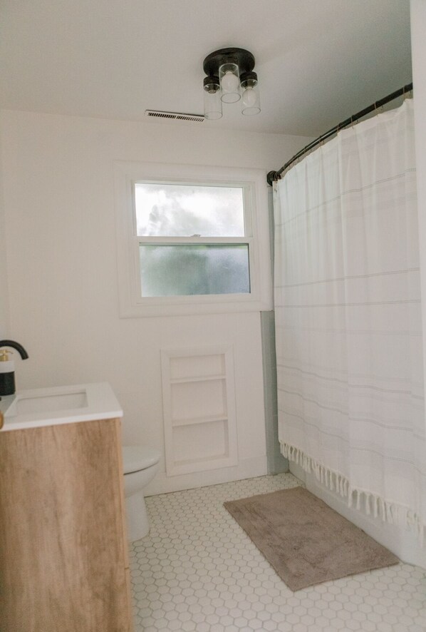 A bathroom with a toilet, a window, a shower curtain, and a white sink. - Beautiful cottage w/pool in bamboo forest! (Central Point)