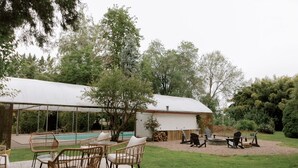 A covered outdoor area with a pool, wicker chairs, and a barbecue setup. - Beautiful cottage w/pool in bamboo forest! (Central Point)