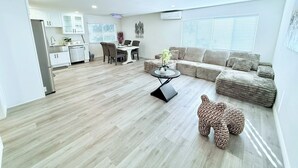 A modern living room with a sofa, a dining table with chairs, a kitchen area, and a decorative elephant statue.
