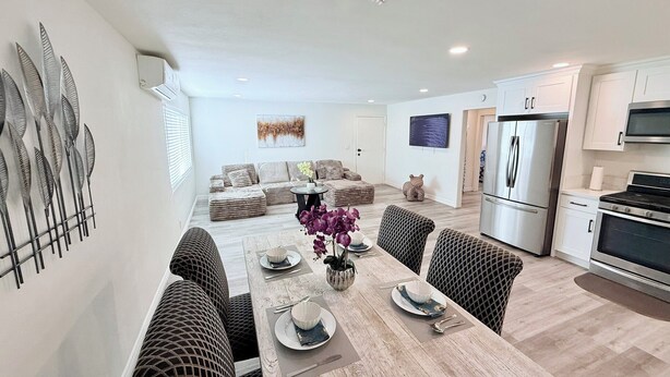 A modern kitchen with stainless steel appliances, a dining area with a wooden table and patterned chairs, and a living area with a sofa and decorative pillows.