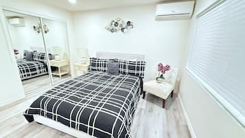 A bedroom with a bed, a chair, a mirror, a wall-mounted air conditioner, and a decorative wall piece.