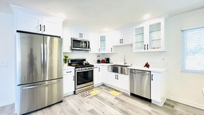 A modern kitchen with white cabinets, stainless steel appliances, and a wooden floor.